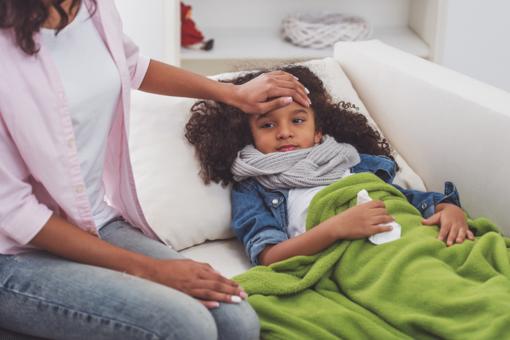 A mother taking care of her sick young daughter who has a cold and putting her hand on the girl’s forehead to feel her temperature in Austin, Texas.